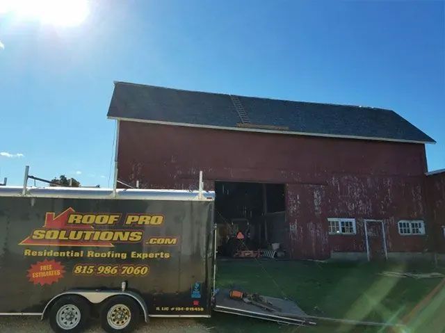 Roof Pro Solutions truck parked by a red barn under a bright blue sky.