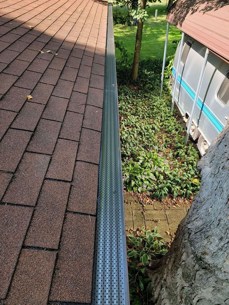 Roof edge with gutter beside a narrow gap between two buildings, showing greenery below.