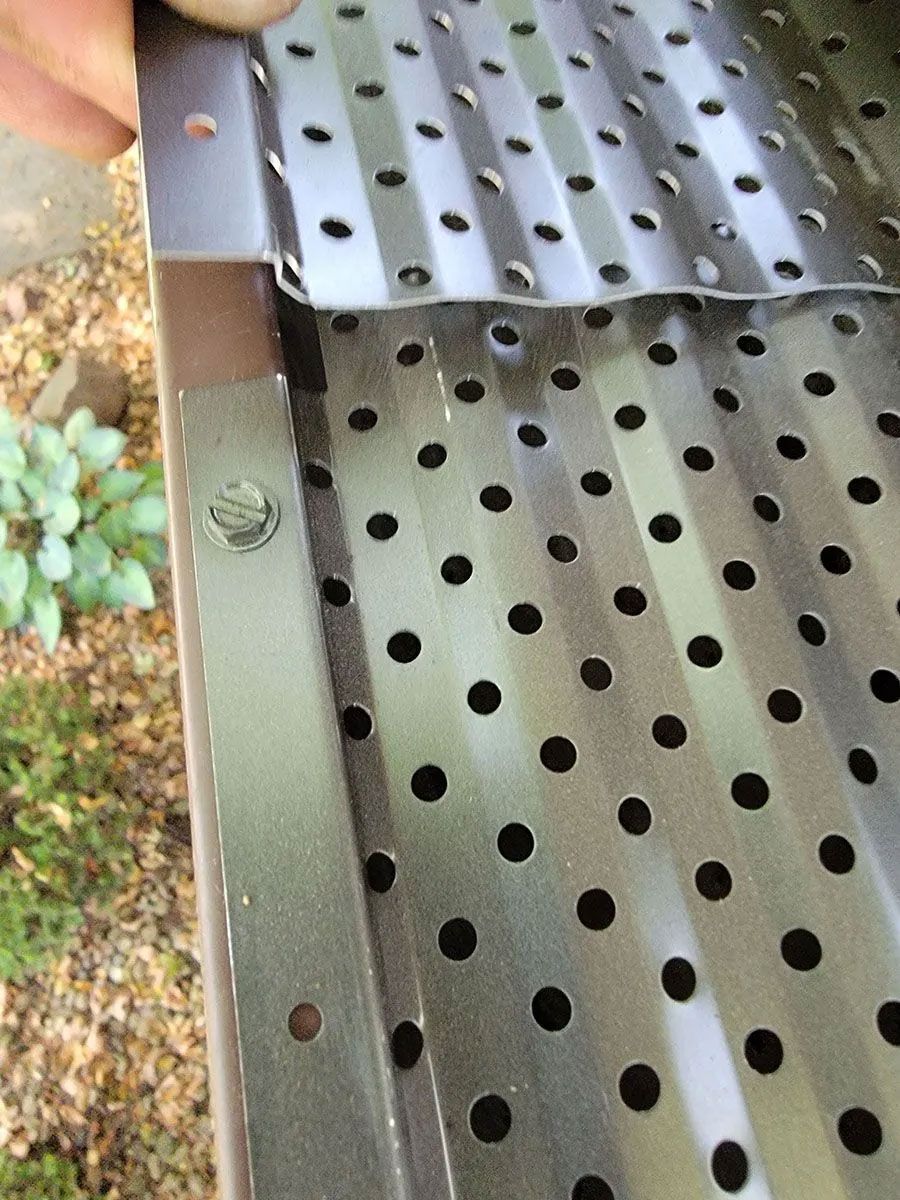Close-up of perforated black metal sheets joined at a corner with screws outdoors.