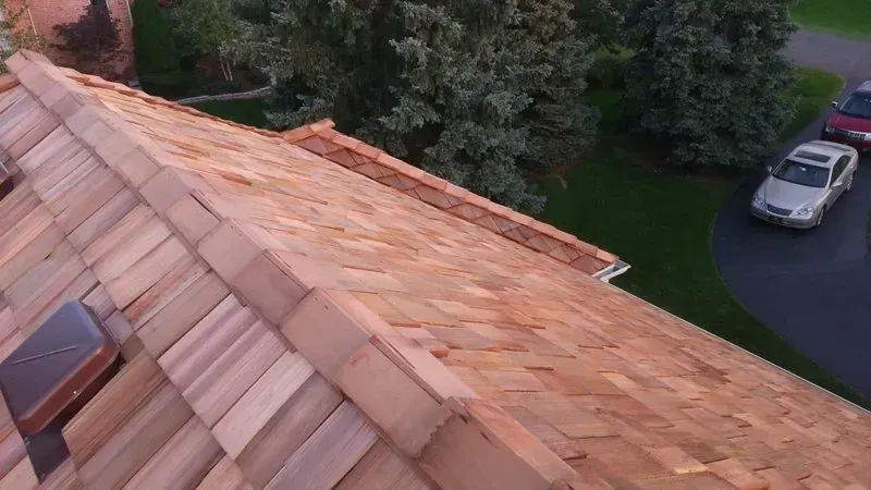 Rooftop with orange shingles beside a driveway and parked white car near trees