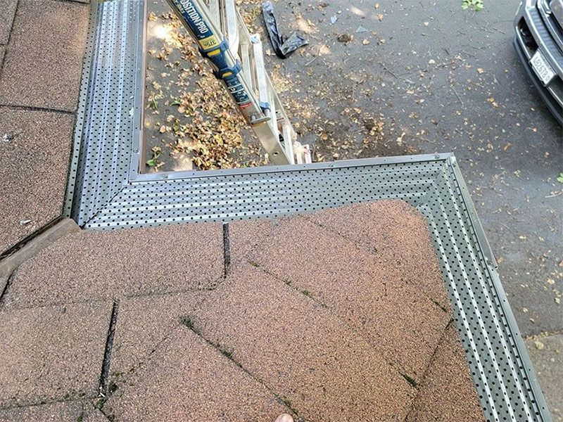 Rooftop edge with brown shingles and metal gutter beside a wet street below.
