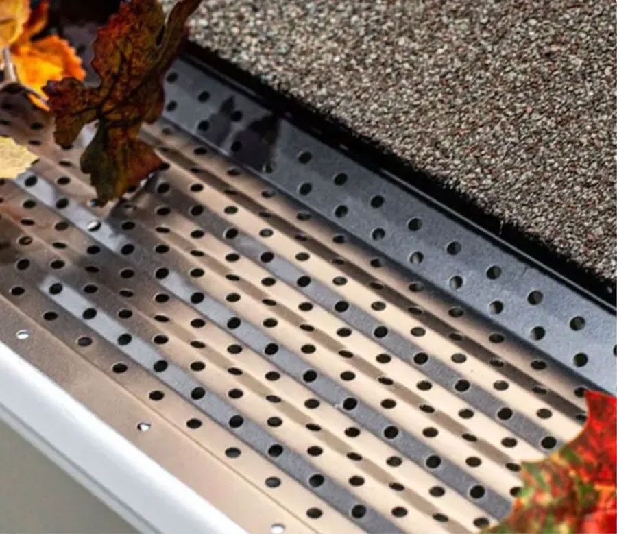 Perforated metal grate with scattered autumn leaves on a speckled surface