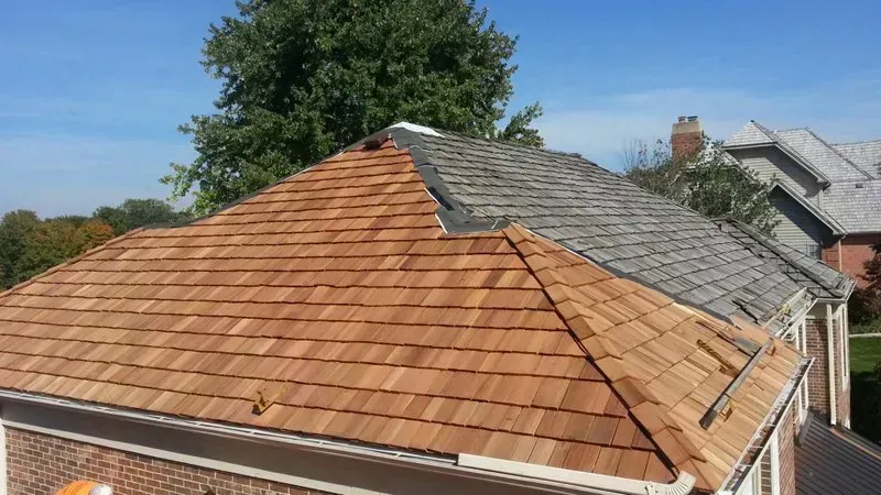 Roof with reddish shingles and a gray patch under repair, viewed above neighboring houses.