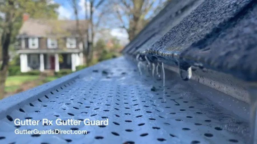 Close-up of black gutter guard on a roof edge with water flowing, house blurred in background