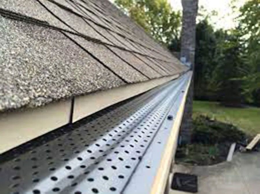 Gutter guard installed along a shingled roof edge beside a house and driveway