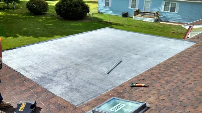 Freshly poured concrete patio beside a brick deck and lawn, with a house and tools visible nearby