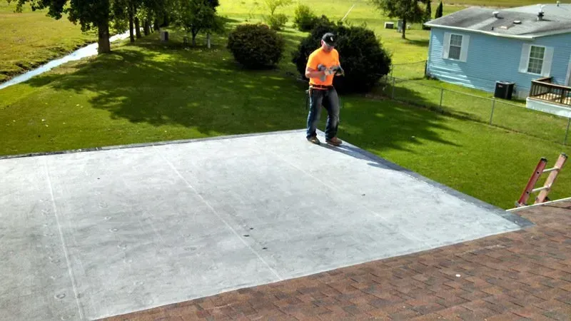 Worker standing on a newly poured concrete driveway beside a house and lawn