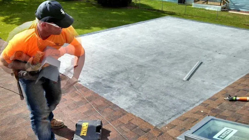 Person in orange shirt and cap working on a brick driveway beside a concrete slab with tools nearby