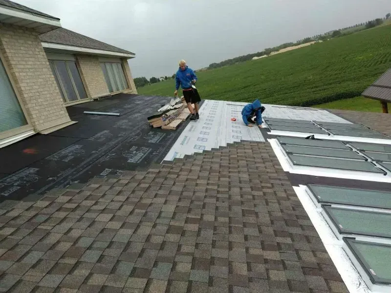 Workers installing roofing on a suburban house beside green fields