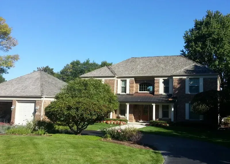 Suburban two-story brick house with a garage, green lawn, and blue sky on a sunny day