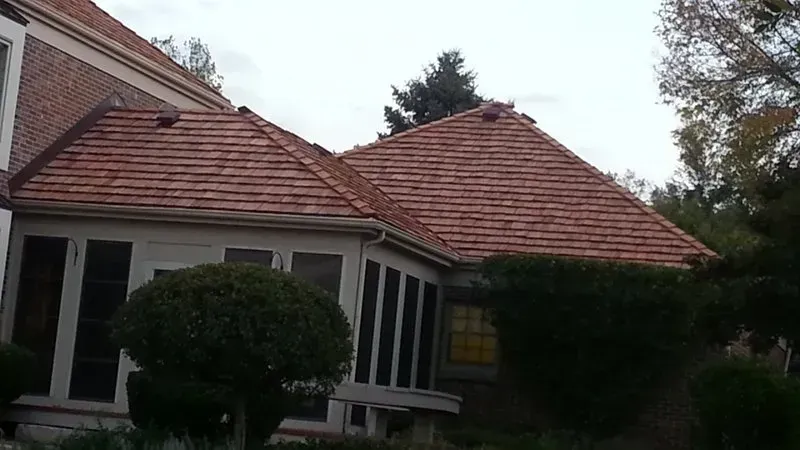 House with red-tiled roof and white trim, seen from a garden with shrubs and trees.