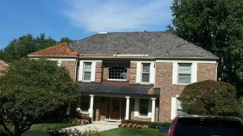 Two-story brick house with a red-tiled roof, front porch, and manicured lawn on a sunny day