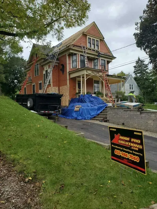 Victorian house under renovation with blue tarp, truck, ladder, and construction sign in front