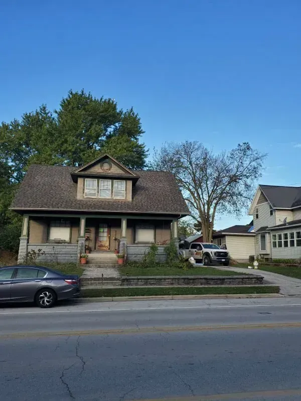 Suburban house with a front porch and steep roof, parked car, and bare trees under a clear blue sky