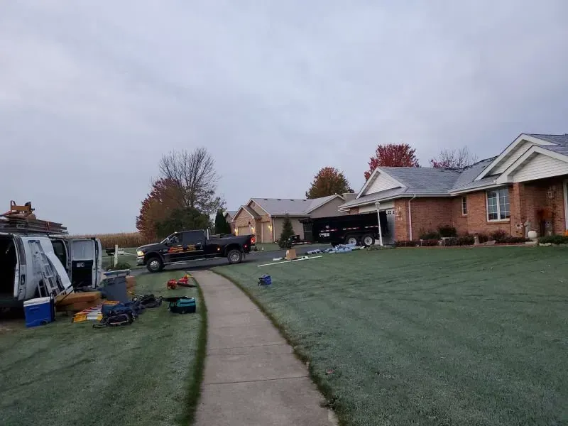 Suburban front yard with a concrete walkway, brick house, parked truck, and yard tools on a cloudy day