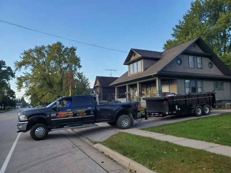Black pickup truck towing a black trailer parked on a residential street beside a house