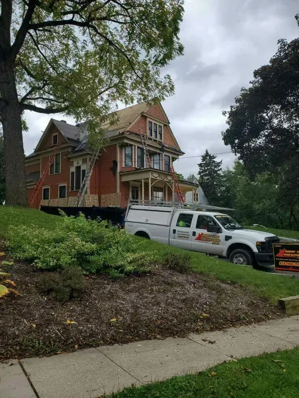 Red brick house on a hillside with a white utility truck parked in front on a cloudy day