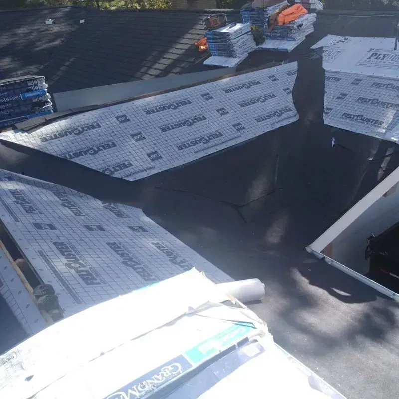 Roof under construction with white panels, dark opening, and stacked materials in sunlight