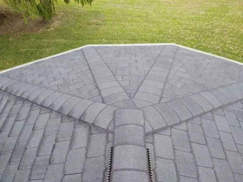 Gray shingled roof with a central ridge and fan-shaped sections, viewed from above against grass.