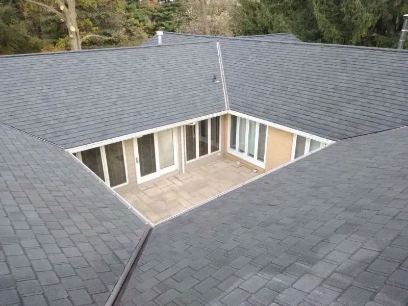 Aerial view of a gray-shingled house roof with a central open courtyard and beige patio below.