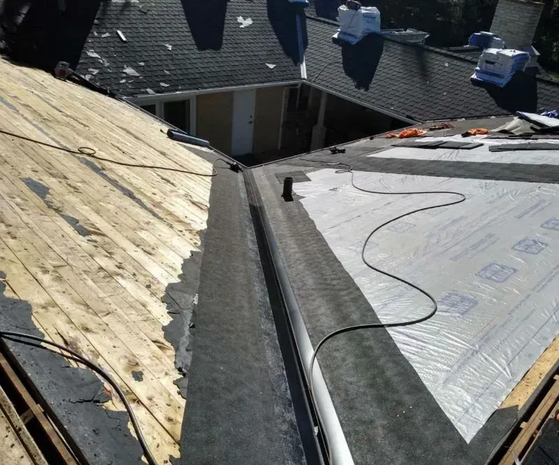 Roof under repair with exposed wood decking and gray underlayment on a steep residential roof.