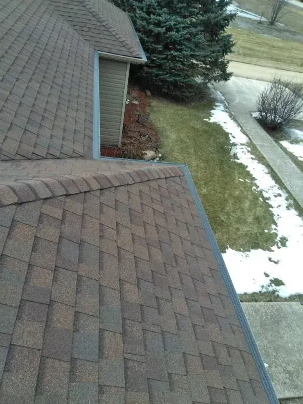 Roof shingles with a snowy yard and walkway beside the house