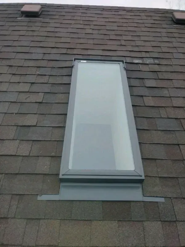 Gray shingled roof with a central ridge and fan-shaped sections, viewed from above against grass.
