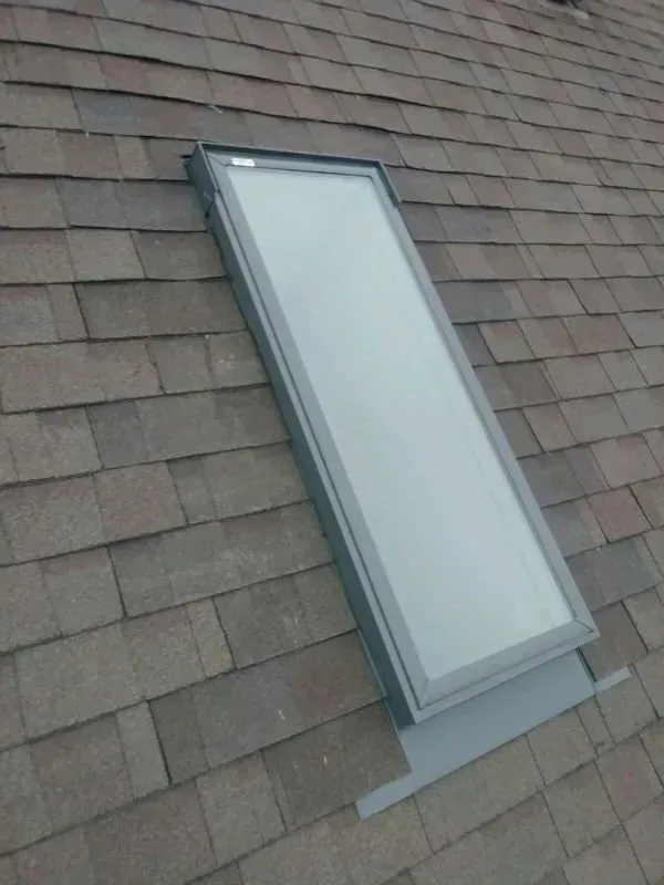 A skylight window set into a gray shingled roof.