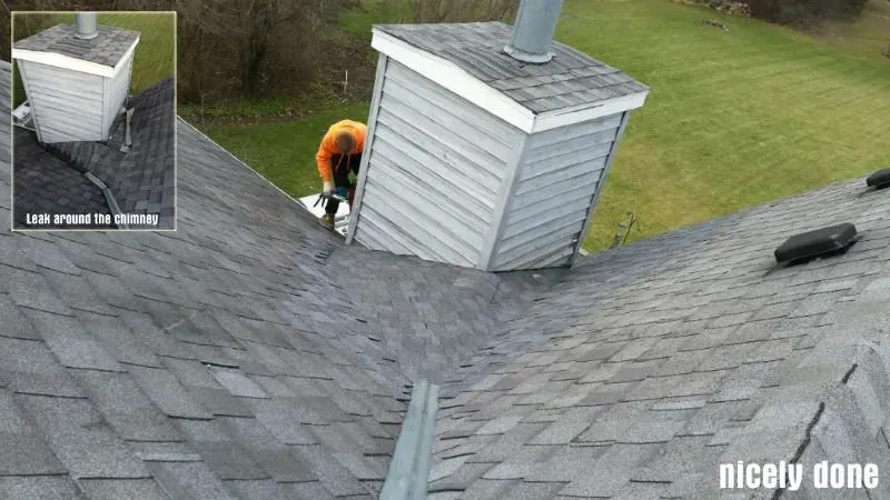 Worker on a roof near a dormer, inspecting shingles beside a chimney.