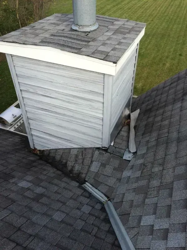 Damaged roof around a white chimney with bent metal flashing and broken shingles