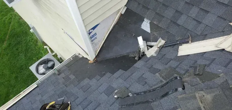 Debris and broken shingles scattered on a rooftop beside a building wall.
