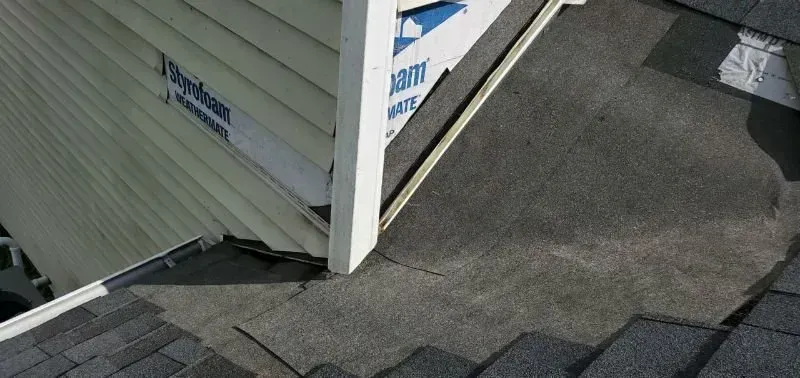 Roof edge and siding corner with shingles, flashing, and a small vent on a sloped roof.