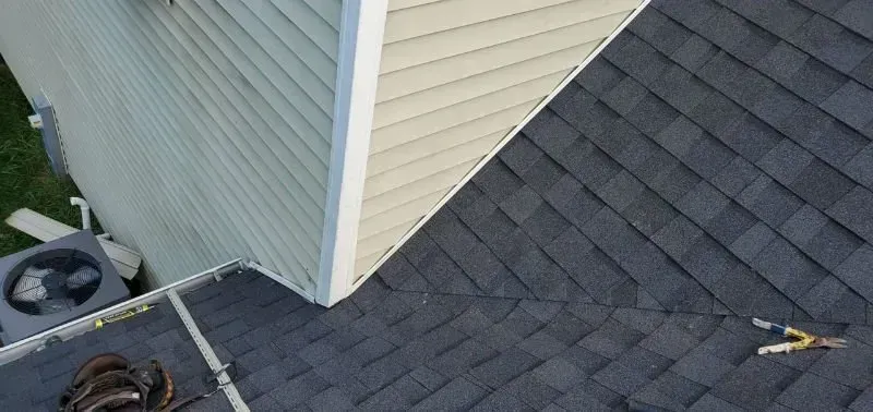 Roof with dark shingles, beige siding, and HVAC units near the edge of a building.