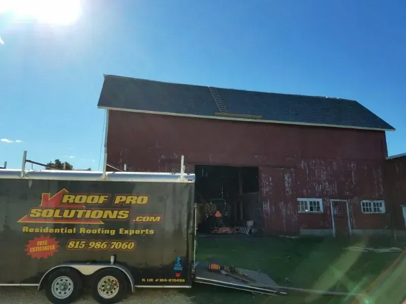 Roof Pro Solutions trailer parked beside a red barn on a sunny day