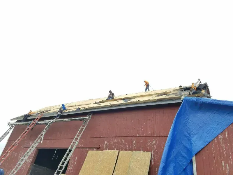 Workers on a red roof under repair, covered partly by a blue tarp and wooden planks.