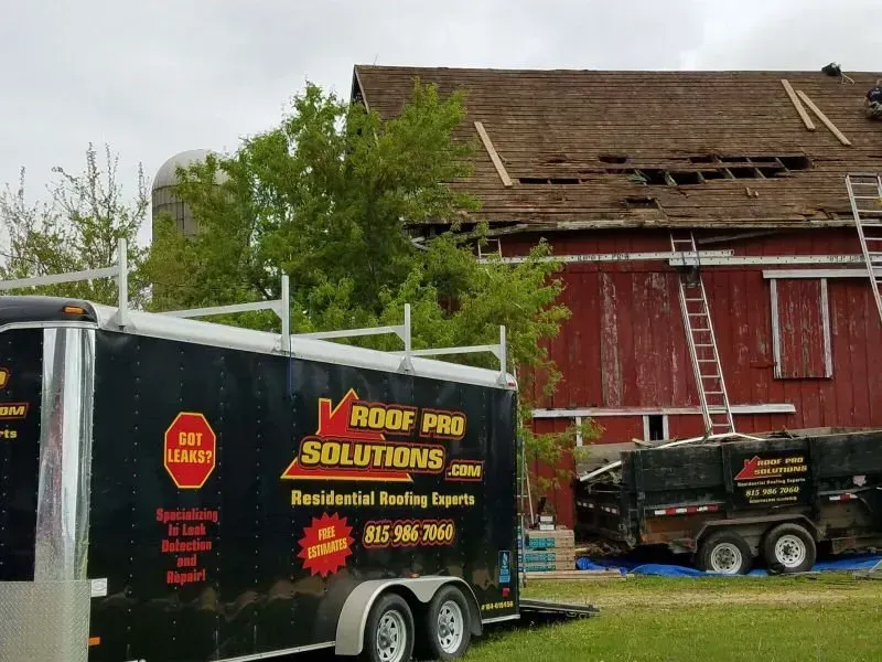 Roofing work in progress on a red barn, with a Roof Pro Solutions truck and trailer in front