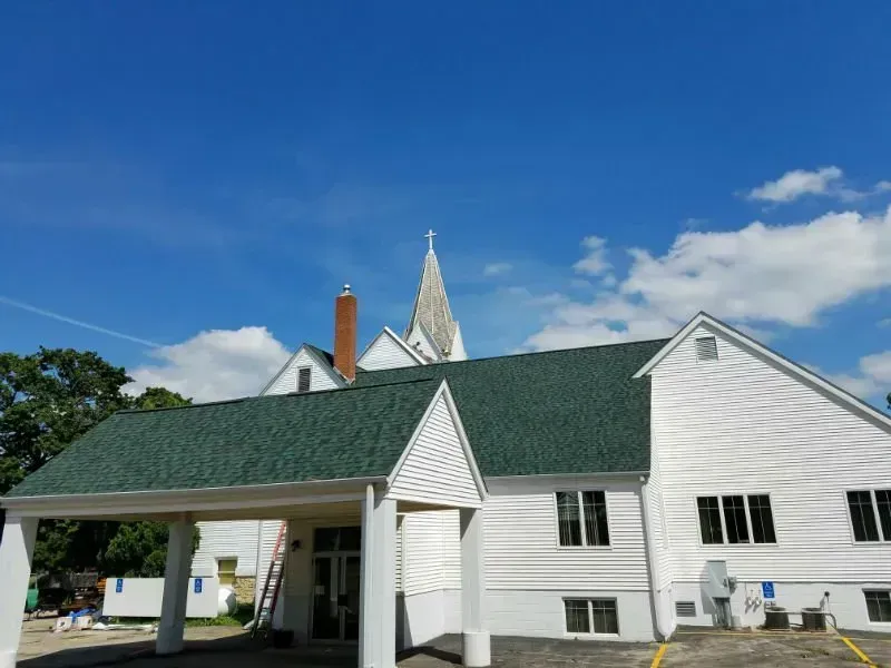 White church building with green roof under a blue sky, with a covered entrance in front