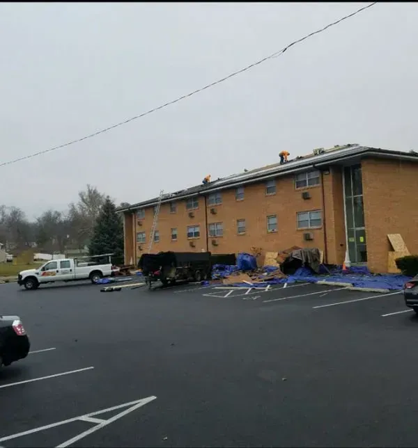 Apartment building with damaged roof and debris in a parking lot after storm damage