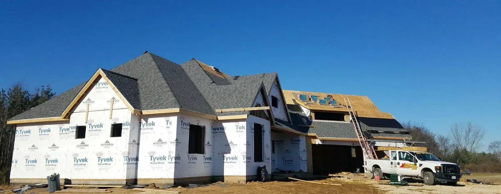 Partially built house with white wrap and dark roof under a clear blue sky