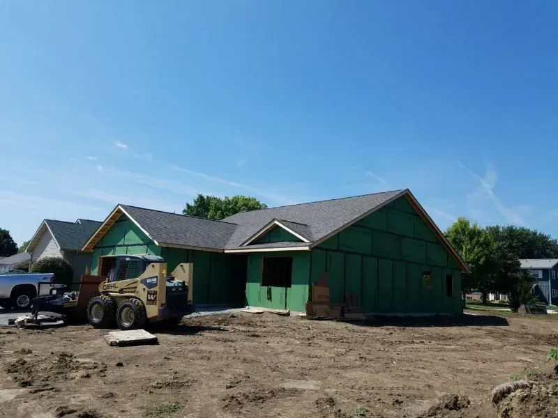 Green house under construction with exposed dirt yard and construction equipment in front
