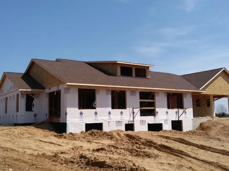Partially built house with brown roof and white siding on a dirt lot under a clear blue sky