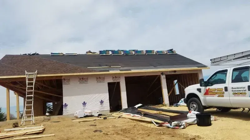 Partially built house with workers' materials, ladder, and a white utility vehicle beside it under a cloudy sky