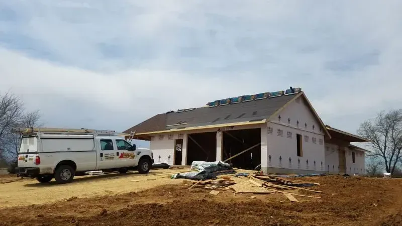 Construction site with a partially built house and a work van on a dirt lot under a cloudy sky