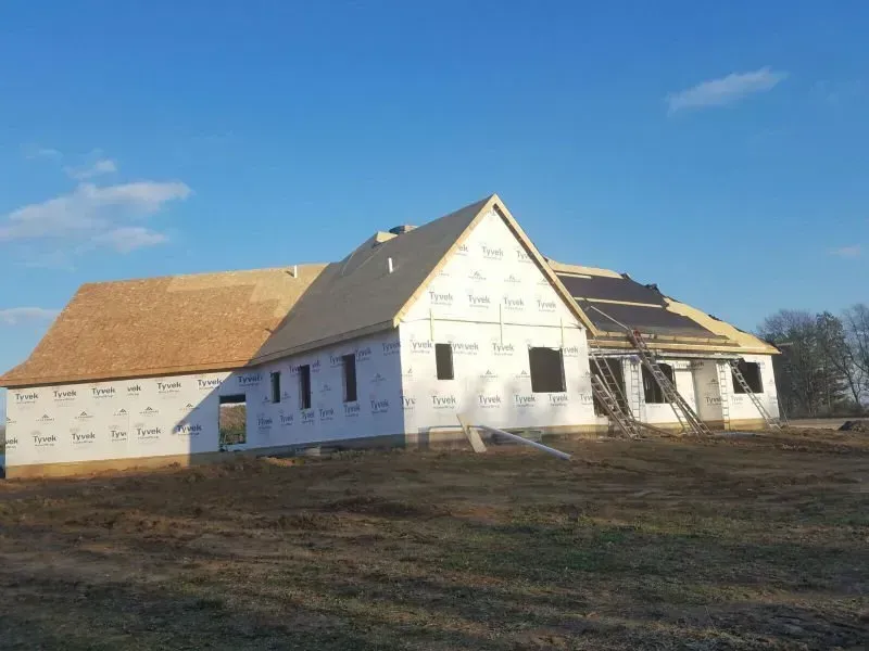 Partly constructed house with white siding and a tan roof under a clear blue sky