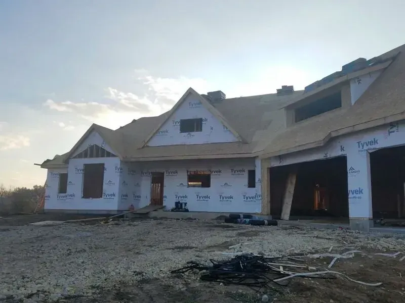 Partially built white house with unfinished roof and open garage on a bare lot at dusk