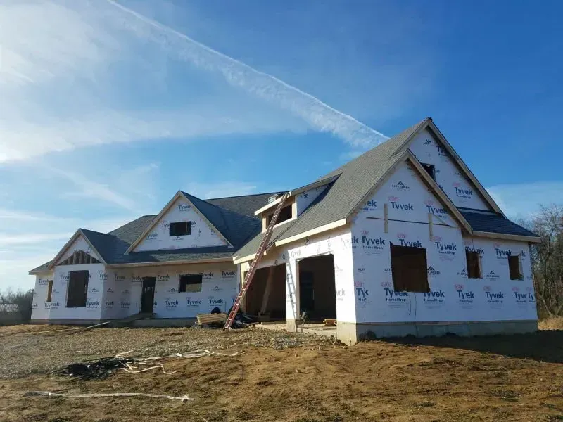 Partially built white house under construction on a dirt lot under a blue sky