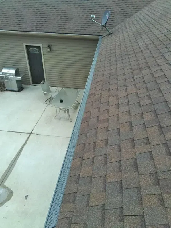 Rooftop view of a patio with two chairs, a grill, and a brick roof slope beside a door