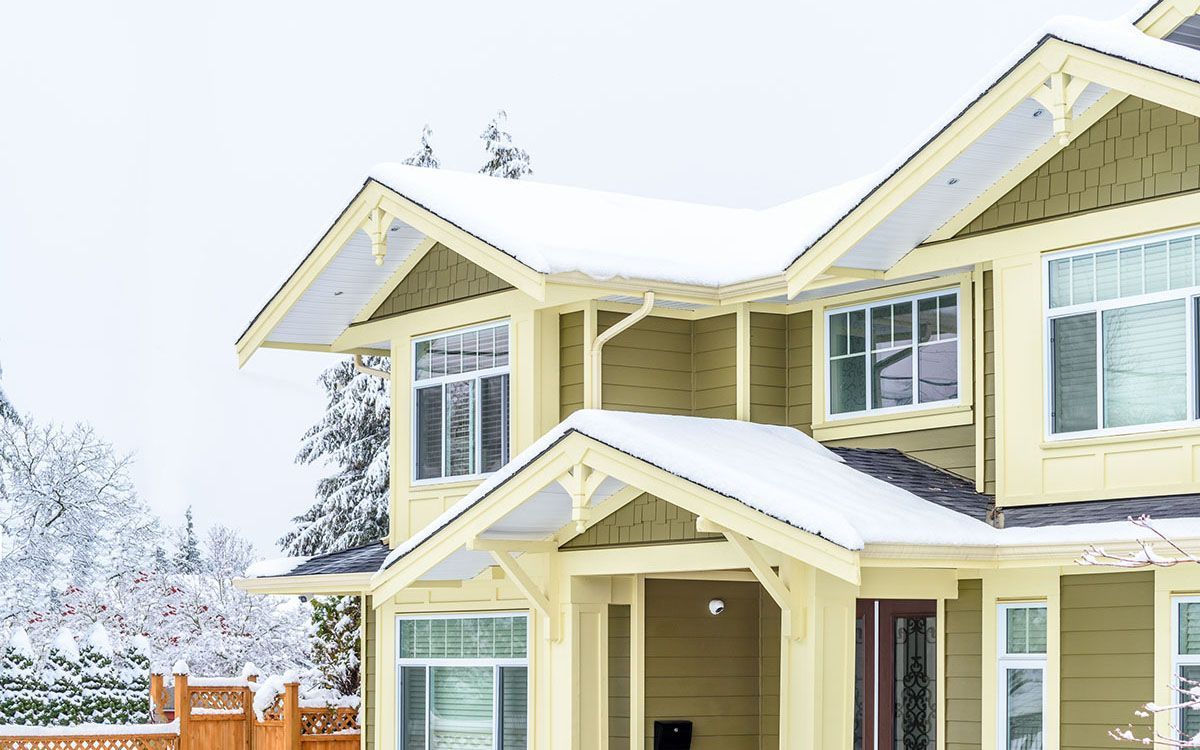 Snow-covered yellow house with white trim and porch in a winter setting