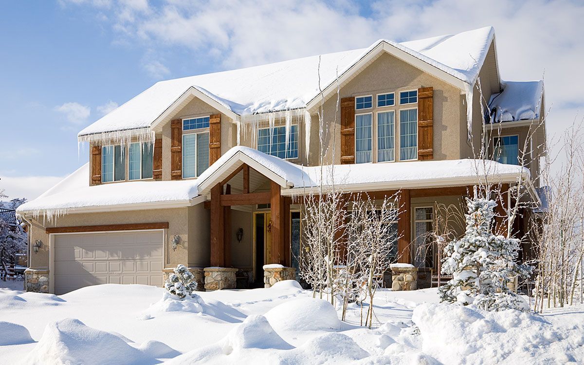 Snow-covered suburban house with a two-car garage and frosty trees in winter sunlight