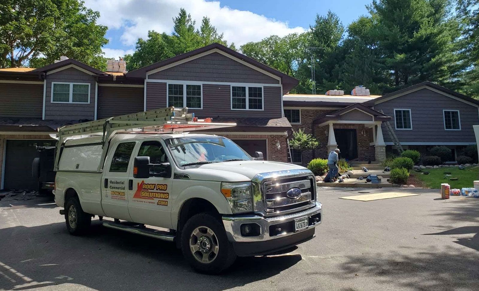 White utility truck parked in front of a house with a front porch and trees in the yard